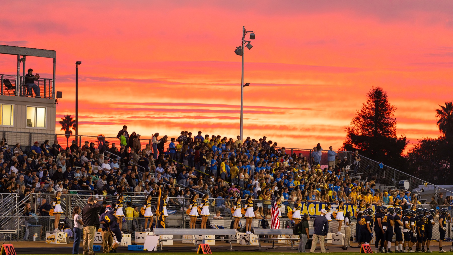 Arroyo Grande fans and the stadium lights beneath an orange and pink sunset before the home opener against Paso Robles