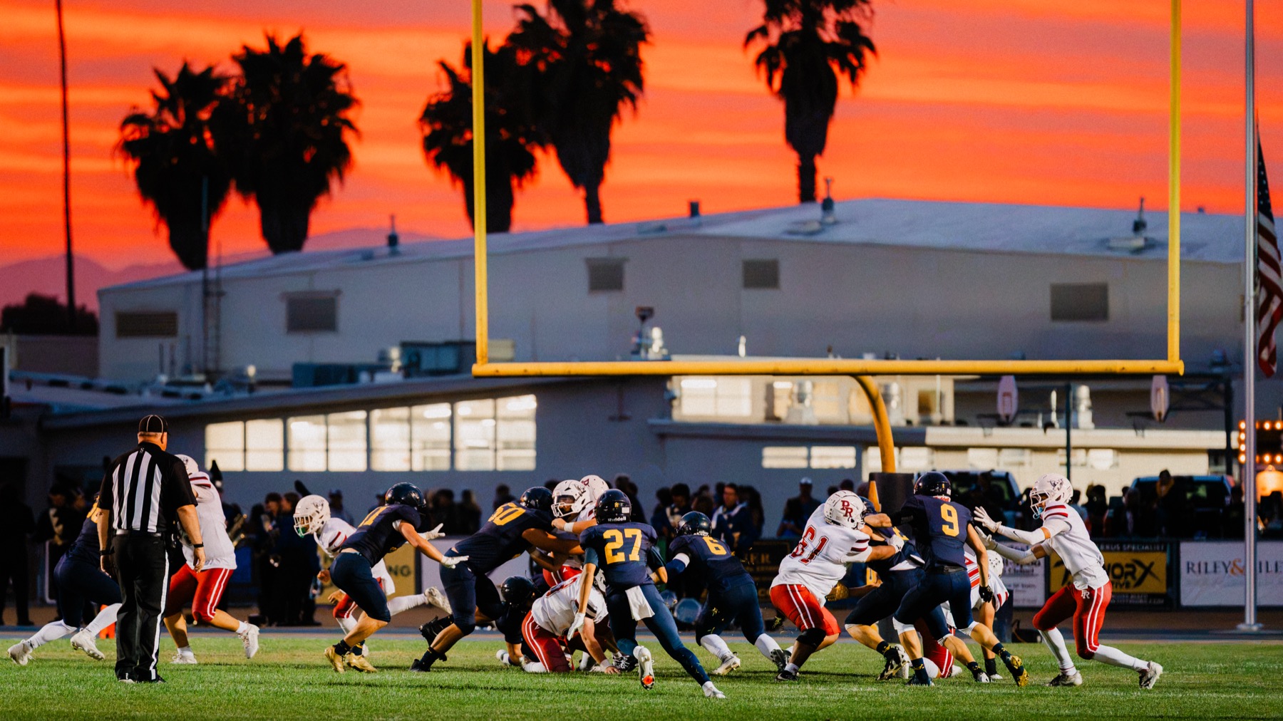 Arroyo Grande and Paso Robles players near the goal line as the sunset silhouettes the goal post and palm trees