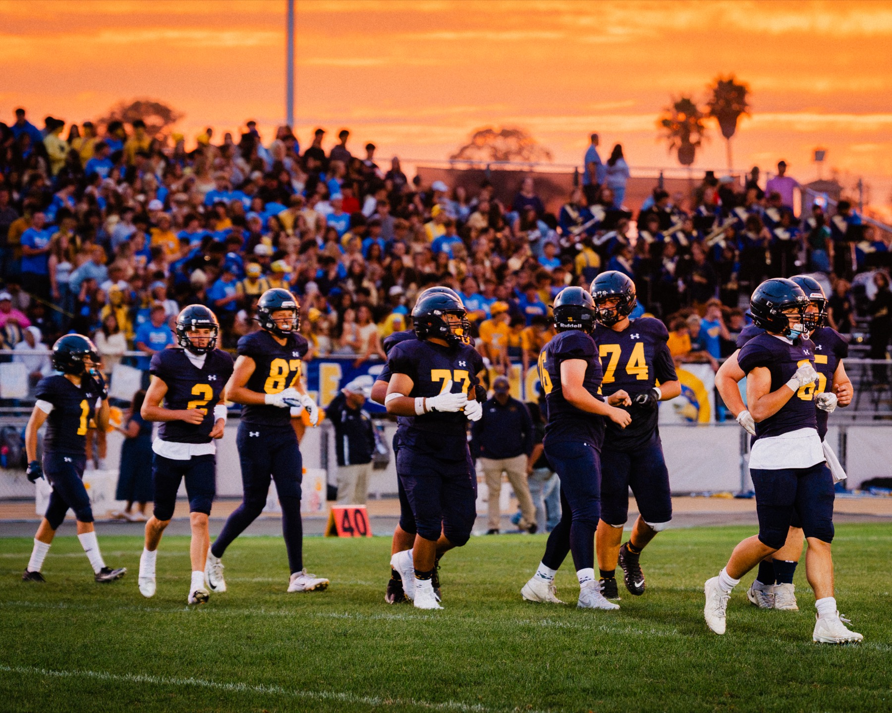 Arroyo Grande players running onto the field under the lights as the sunset fades and the crowd cheers