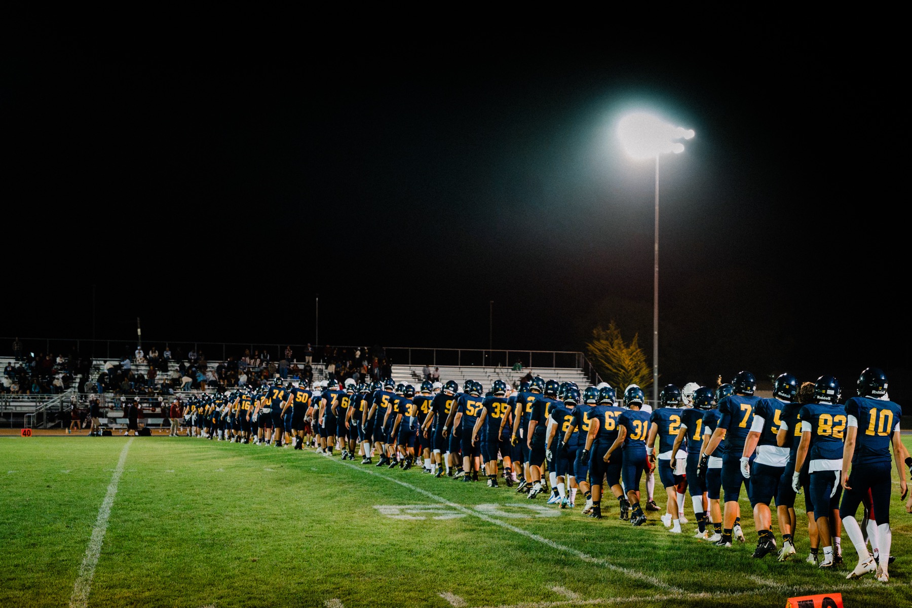 An Arroyo Grande coach walks the sideline under the stadium lights