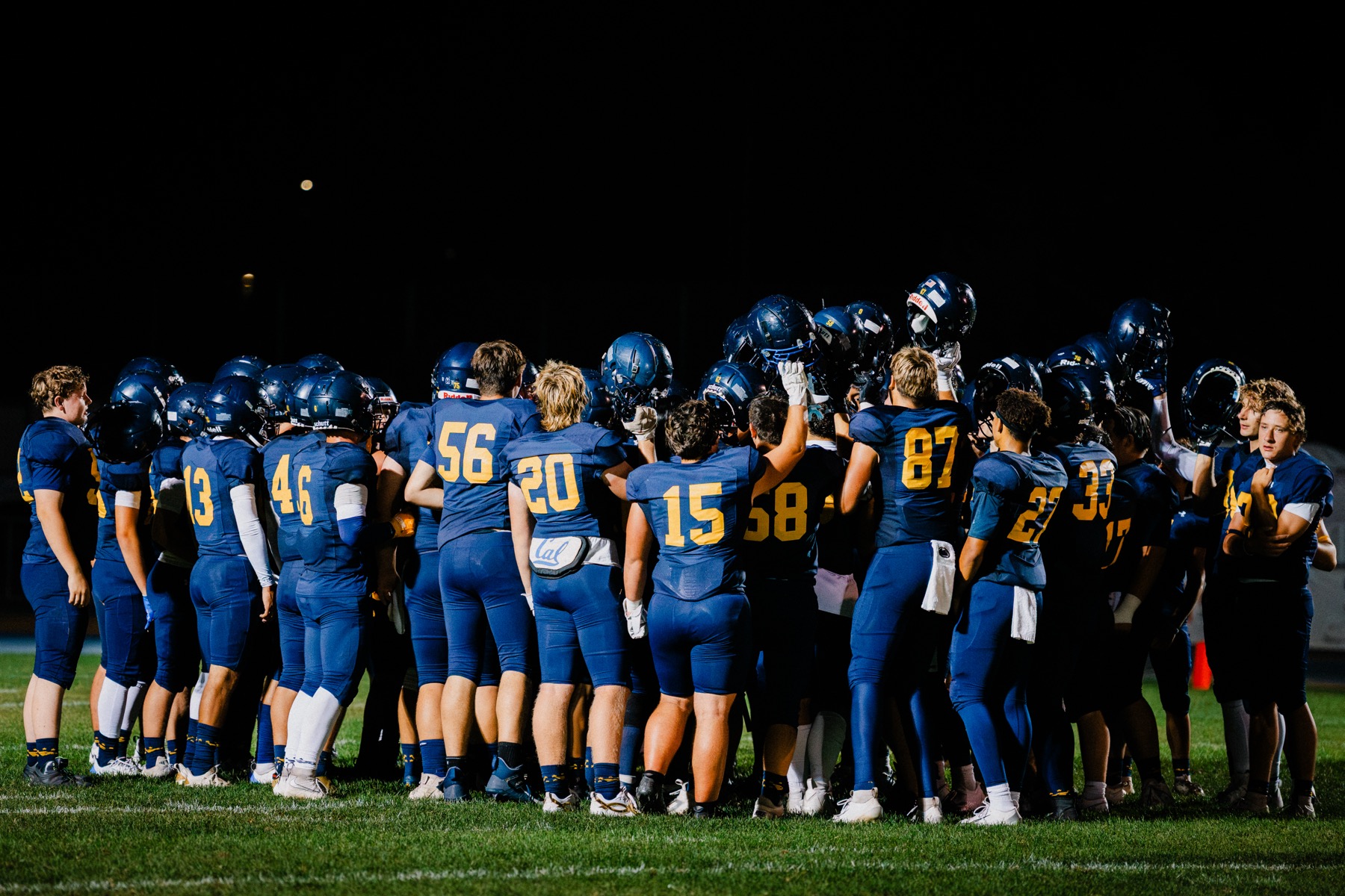 Arroyo Grande players in formation along the sideline, numbers lit under the stadium lights